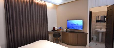 A hotel room with a bed, a desk with a television, a small chair, and a bathroom visible through an open door.