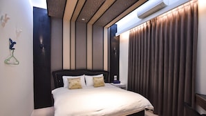 Une chambre d’hôtel moderne, dotée d’un grand lit, d’une table de chevet, d’un climatiseur fixé au mur et offrant une vue sur l’extérieur par la fenêtre.