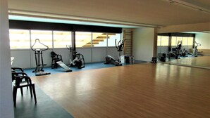 Une salle de sport spacieuse, dotée de divers appareils d’exercice, de grandes fenêtres et d’un plancher en bois.