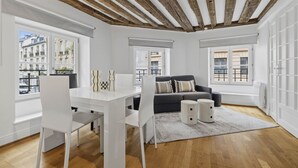 Una sala de estar moderna con una mesa de comedor blanca, sillas, un sofá gris y un tapete blanco.