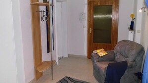 A living room with a grey sofa, a wooden shelf with hanging items, a door with a glass panel, and a small table with a vase. - Self-in Goslar, suitor Apartment - Erdgescschoss (Goslar)
