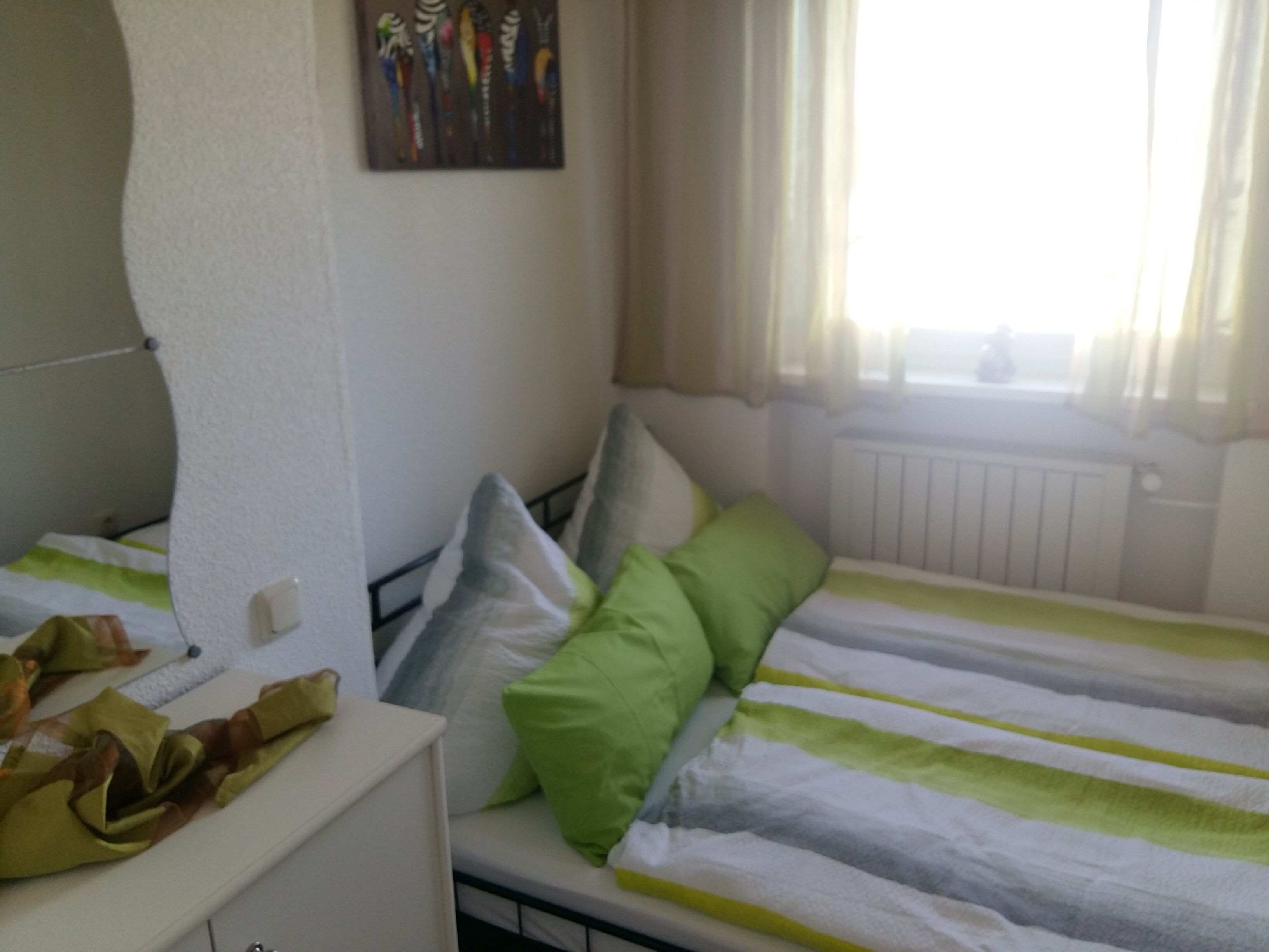 Une chambre d’hôtel avec deux lits, une commode blanche, un tableau au mur et une fenêtre avec des rideaux.