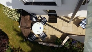 A patio with a round table and six striped chairs, surrounded by a wooden deck and a small garden area. - Self-in Goslar, suitor Apartment - Erdgescschoss (Goslar)