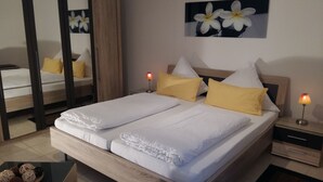 A neatly made double bed with white linens and yellow pillows, a bedside table with a lamp, and a wall-mounted mirror. - Self-in Goslar, suitor Apartment - Erdgescschoss (Goslar)