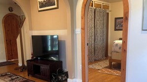 Un salon doté d’un téléviseur à écran plat, d’un meuble de rangement en bois et d’un grand tapis à motifs.