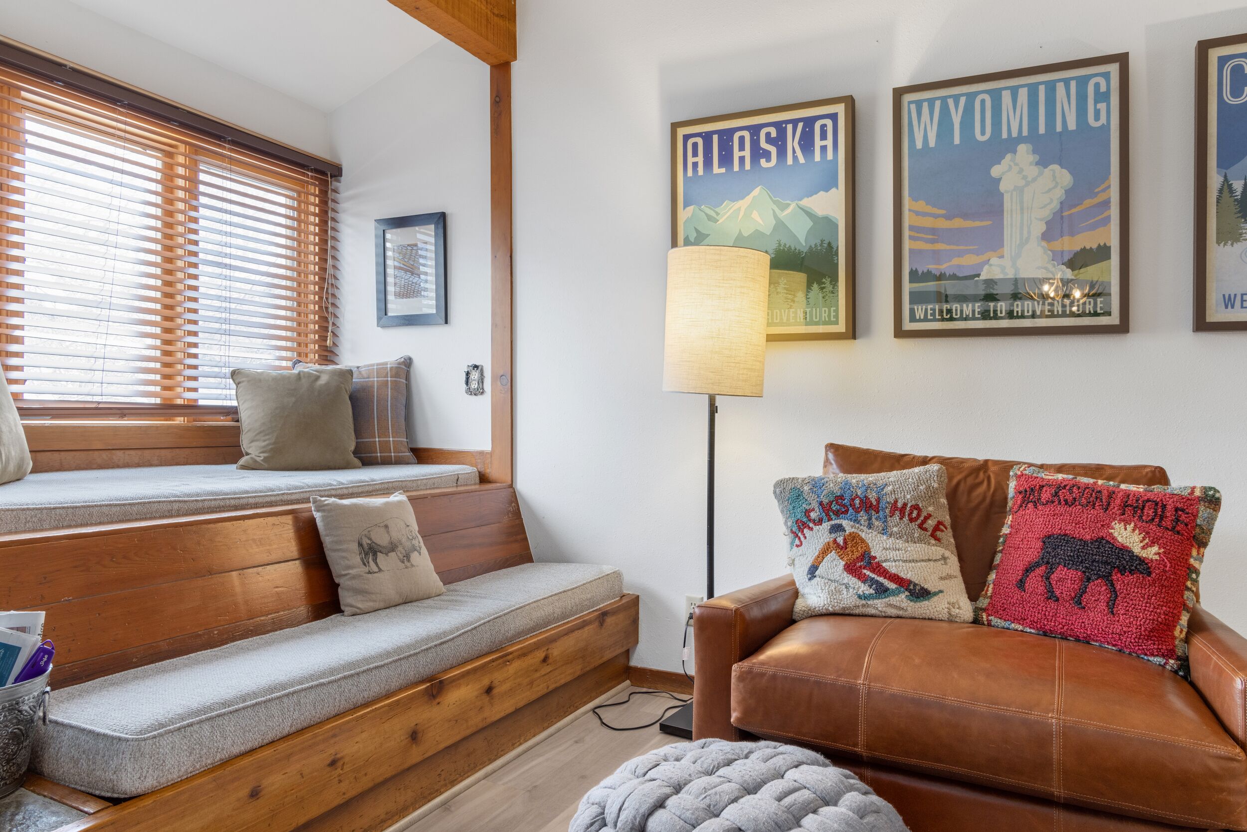 Un salon chaleureux avec un banc en bois, un canapé en cuir et une lampe. Les murs sont décorés de tableaux, dont des affiches représentant l’Alaska et le Wyoming.