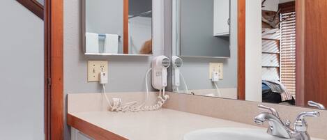 A bathroom with a wooden vanity, a sink, a mirror, and a hairdryer plugged in.