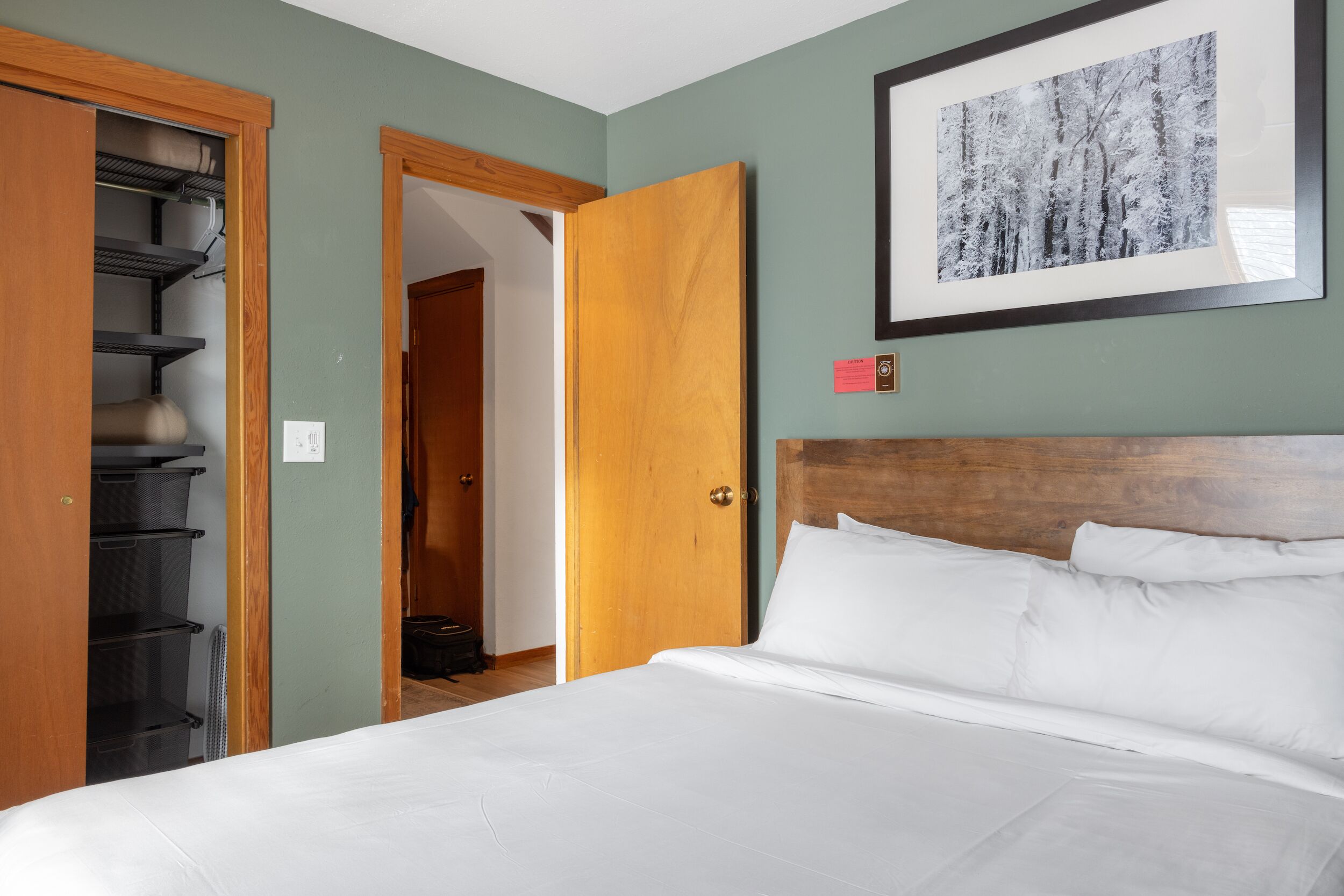 Un dormitorio con una cama, cabecera de madera, un cuadro enmarcado en la pared y un armario con estantes.