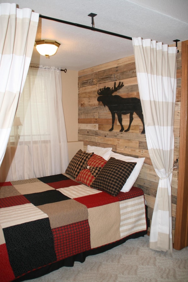 A bed with a quilt, curtains, and a wall-mounted moose picture.