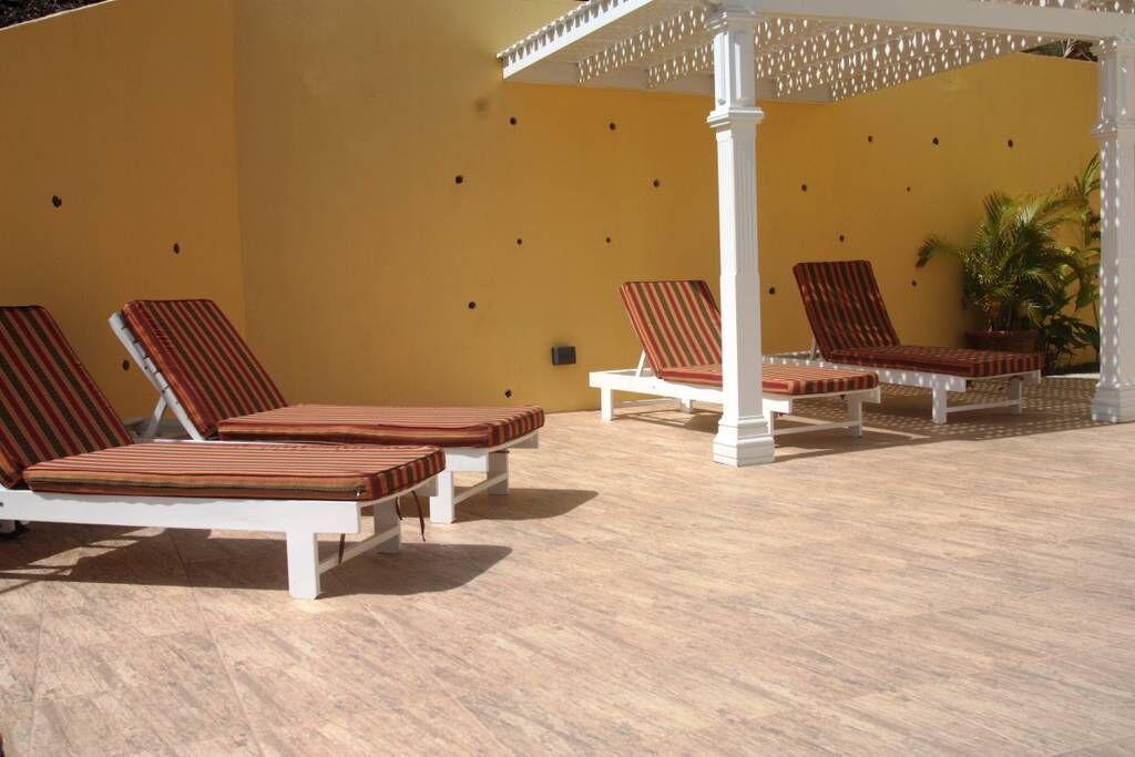 A sunlit outdoor lounge area with white lounge chairs and a pergola.