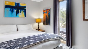 A hotel room with a large bed, two paintings, a window with curtains, and a lamp. - Outpost: Geranium 2622 (Wilson)
