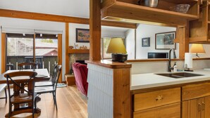 A kitchen with wooden cabinets, a sink, and a dining area with chairs and a table. - Outpost: Geranium 2622 (Wilson)