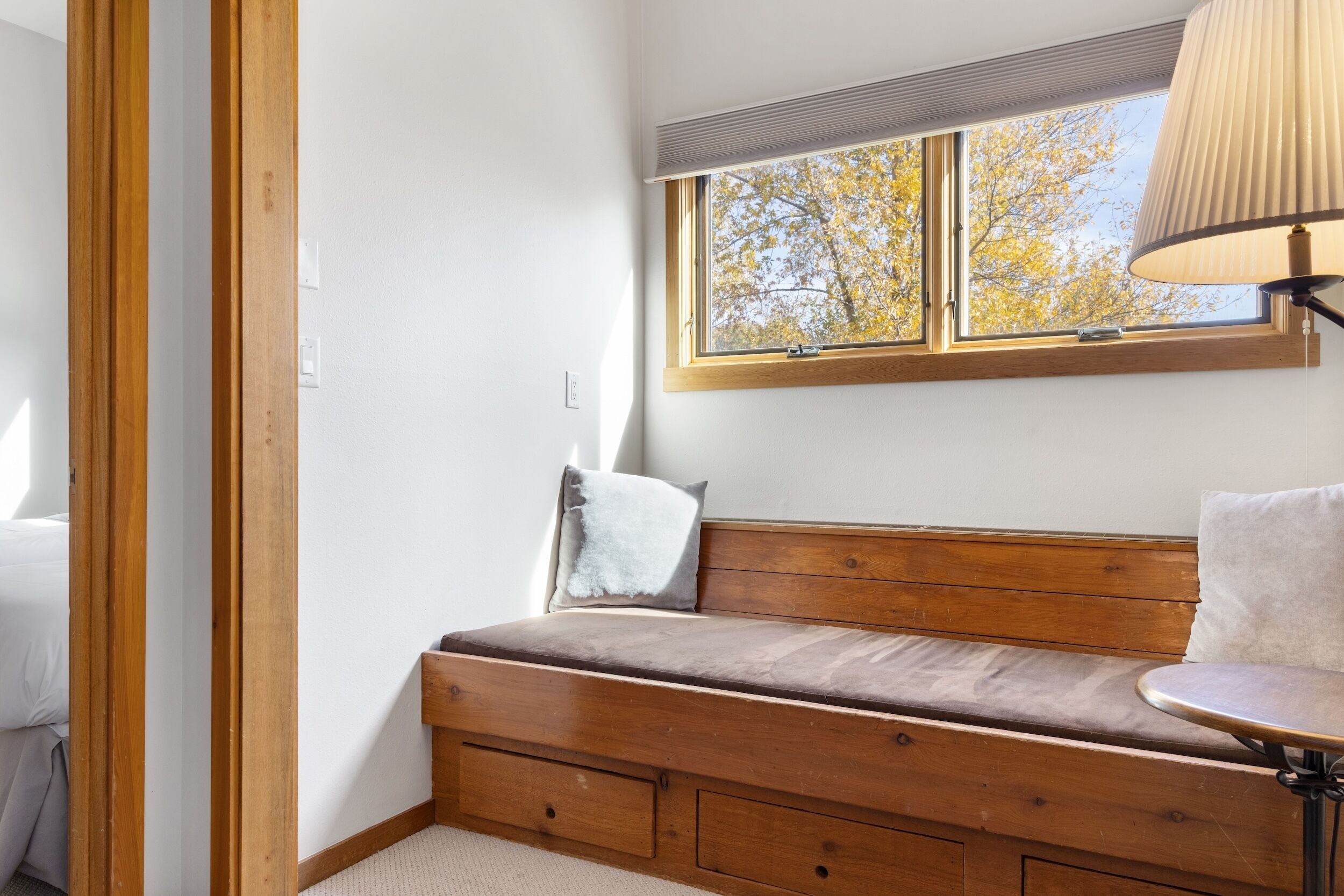 Una habitación acogedora con un banco de madera, una mesita y un ventanal con vistas a árboles.