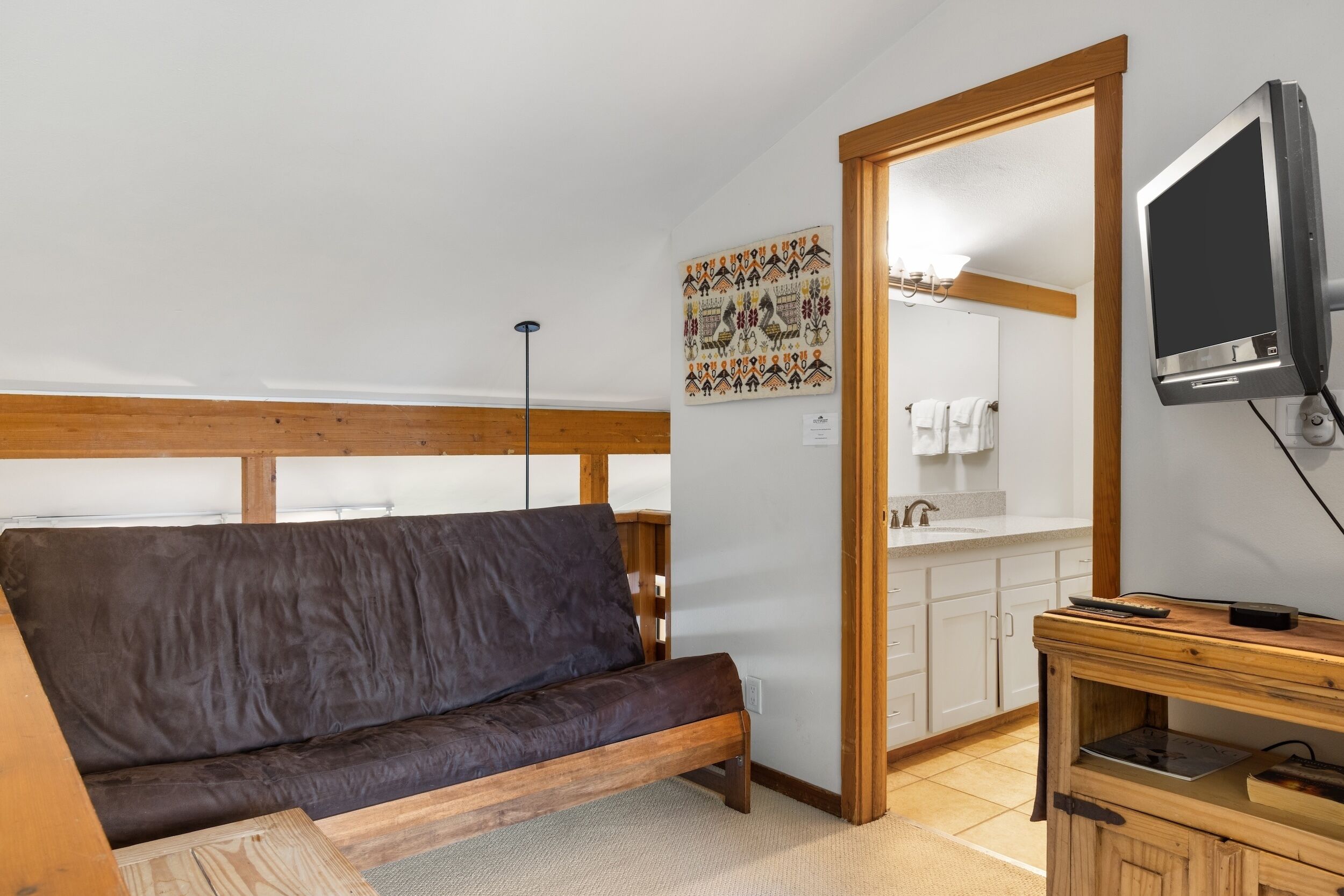 Ein gemütliches Zimmer mit einer hölzernen Bank, einem Fernseher, einem Holzschrank und einem durchgegangenen Tür sichtbar liegenden Badezimmer.