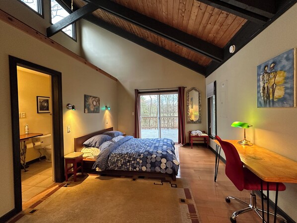 Een slaapkamer met een bed, een bureau, een stoel, een raam en een schilderij aan de muur.