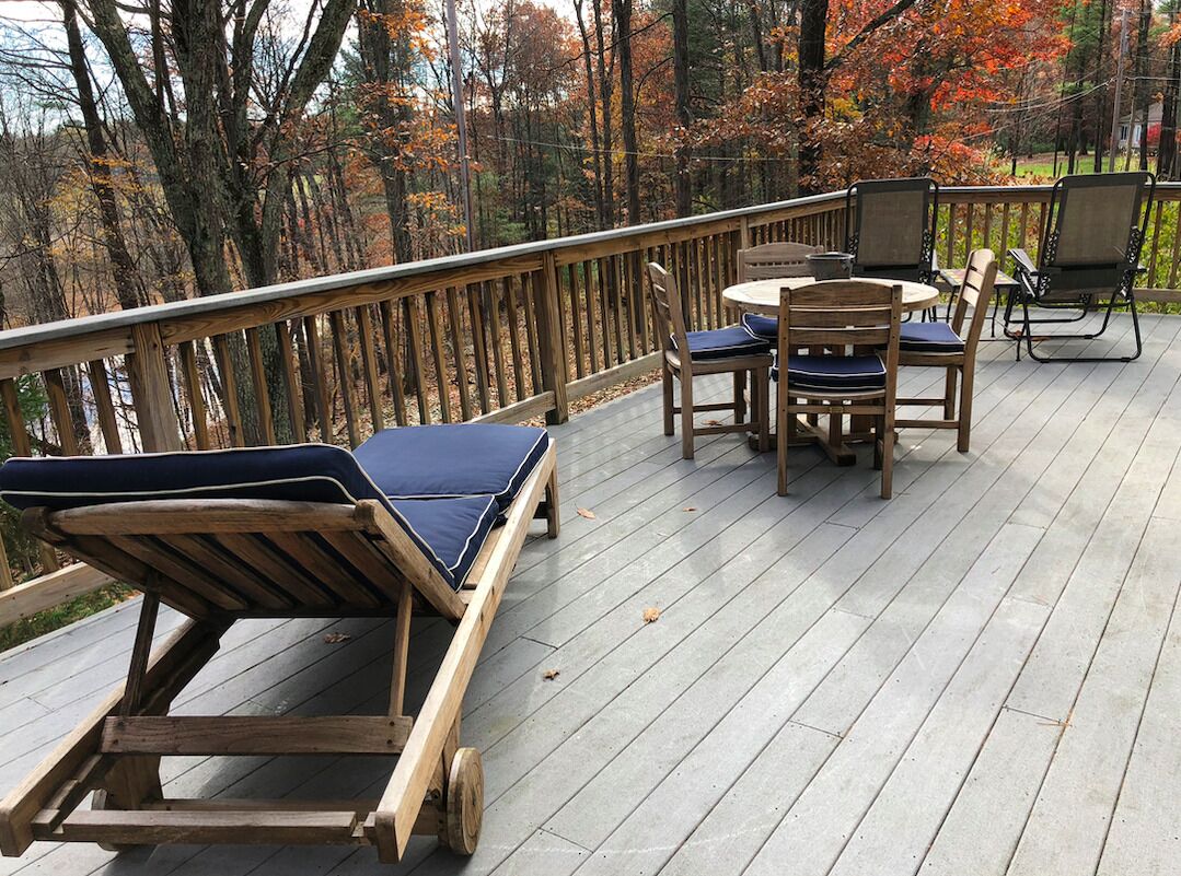 A wooden deck with lounge chairs and a table, surrounded by trees with autumn foliage.