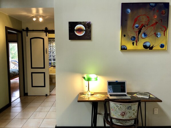 Una habitación con escritorio, silla, computadora portátil, lámpara y dos obras de arte en la pared.