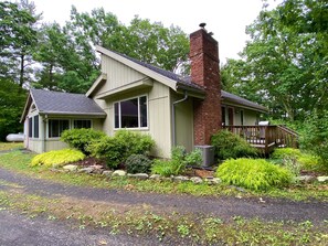 A single-story house with a brick chimney, a porch with a wooden railing, and a small attached garage.