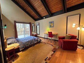 A bedroom with a bed, a desk, a red chair, a red sofa, and a large window with blinds.
