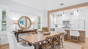 Comedor con una mesa y sillas de madera, un espejo grande y vista a la cocina.