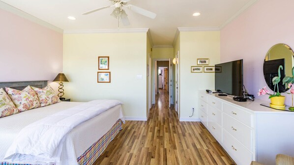 Un dormitorio con cama, lámpara de noche, cómoda, televisor y un pasillo que conduce a otra habitación.