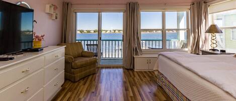 Een hotelkamer met een groot bed, een televisie, een bank en een balkon met uitzicht op zee.