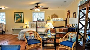 Une pièce accueillante avec un lit, deux fauteuils en osier, une petite table avec une lampe, une pancarte « Bienvenue » et un tapis décoré d’une étoile de mer.