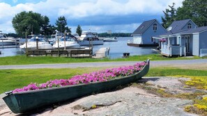 Ein Bootssteg mit einem Blumenboot im Vordergrund, ein Haus mit Satellitenschüssel und mehrere Boote im Hintergrund.