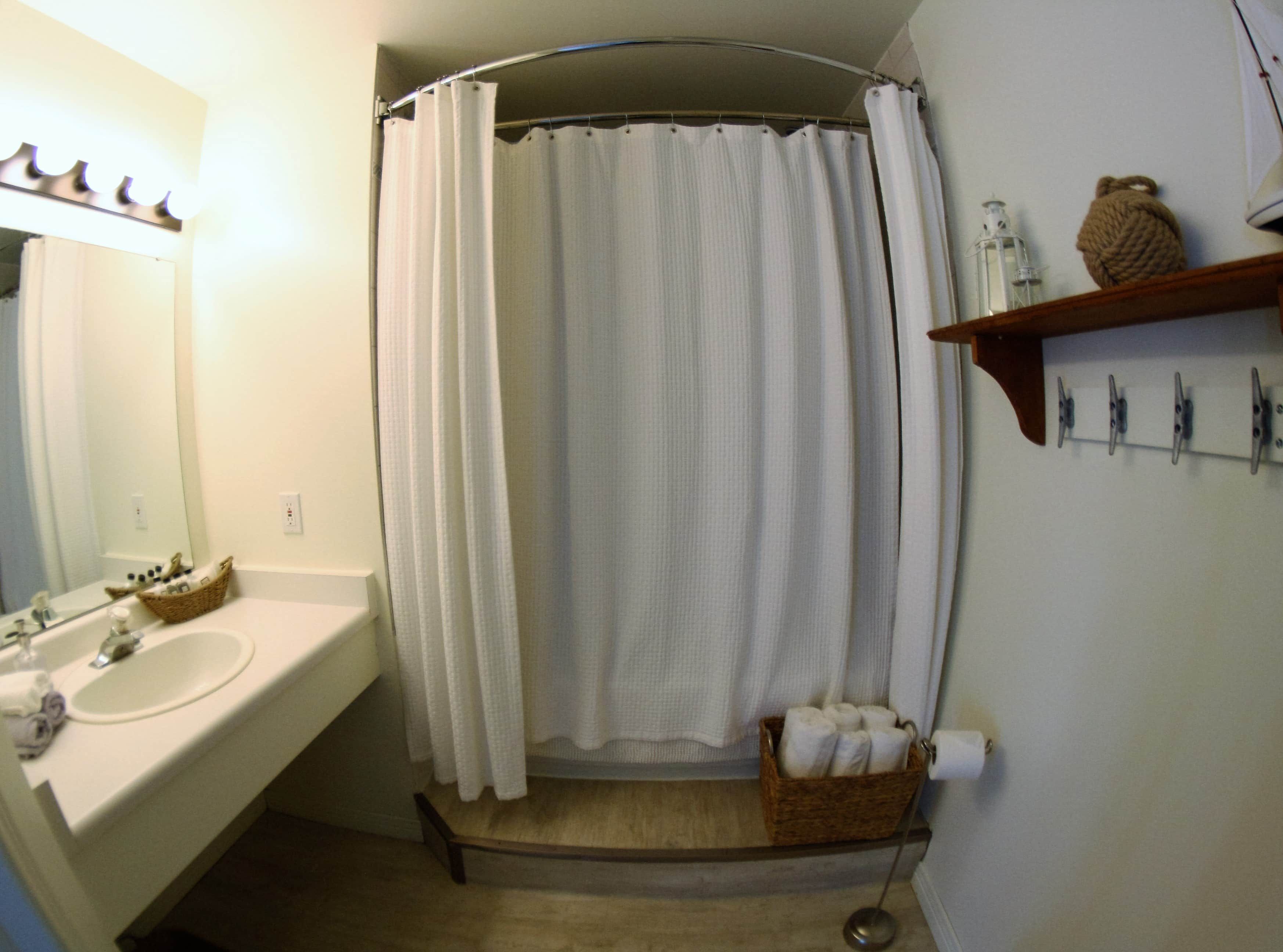 A bathroom with a white sink, a mirror, a shower curtain, a towel rack, and a basket of towels.