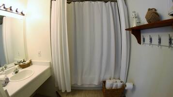 A bathroom with a white sink, a mirror, a shower curtain, a towel rack, and a basket of towels.