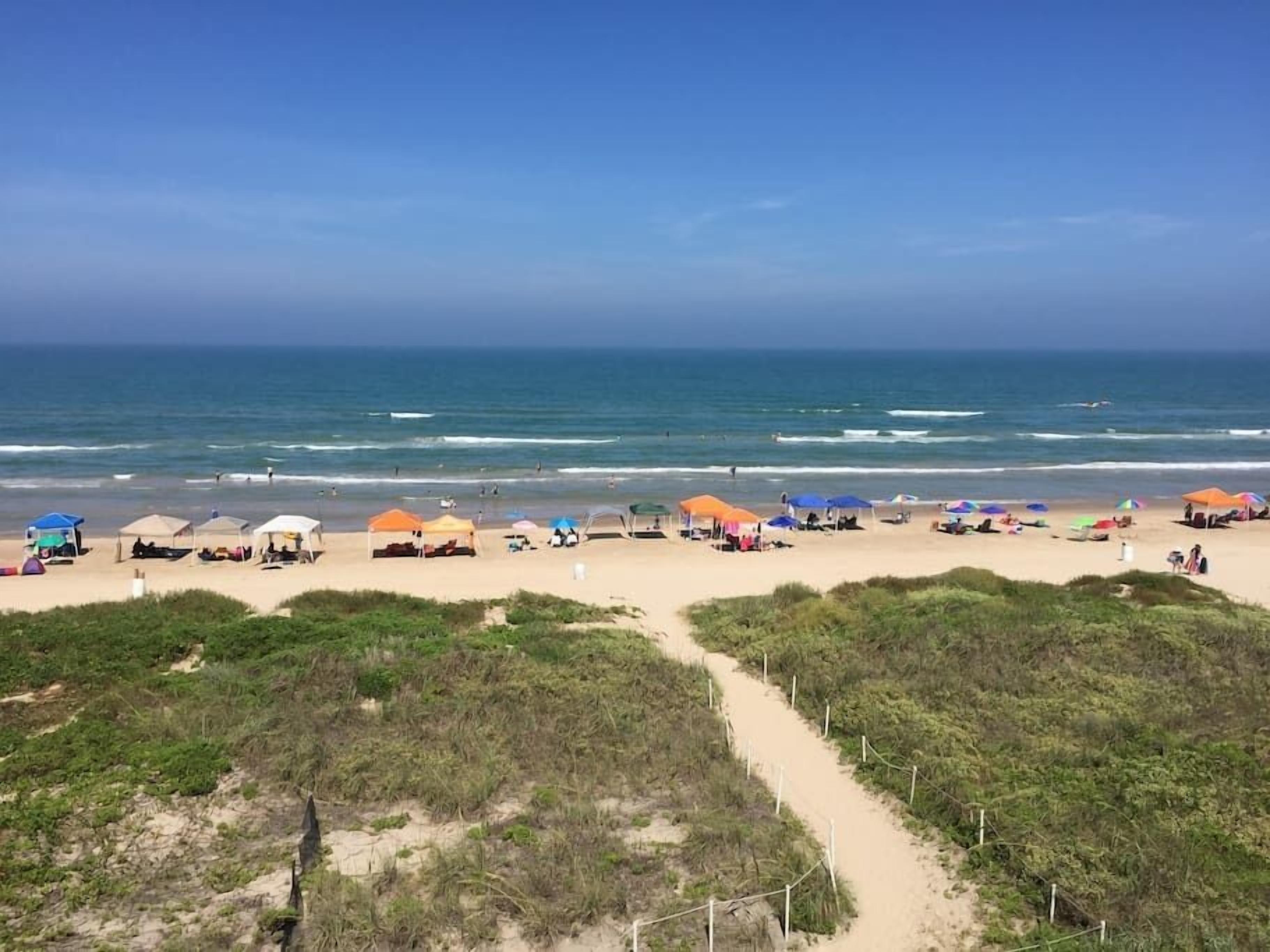 Een strand met tenten en parasols, een zandpad en de oceaan op de achtergrond.