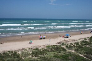 A beach with people, umbrellas, and dunes.