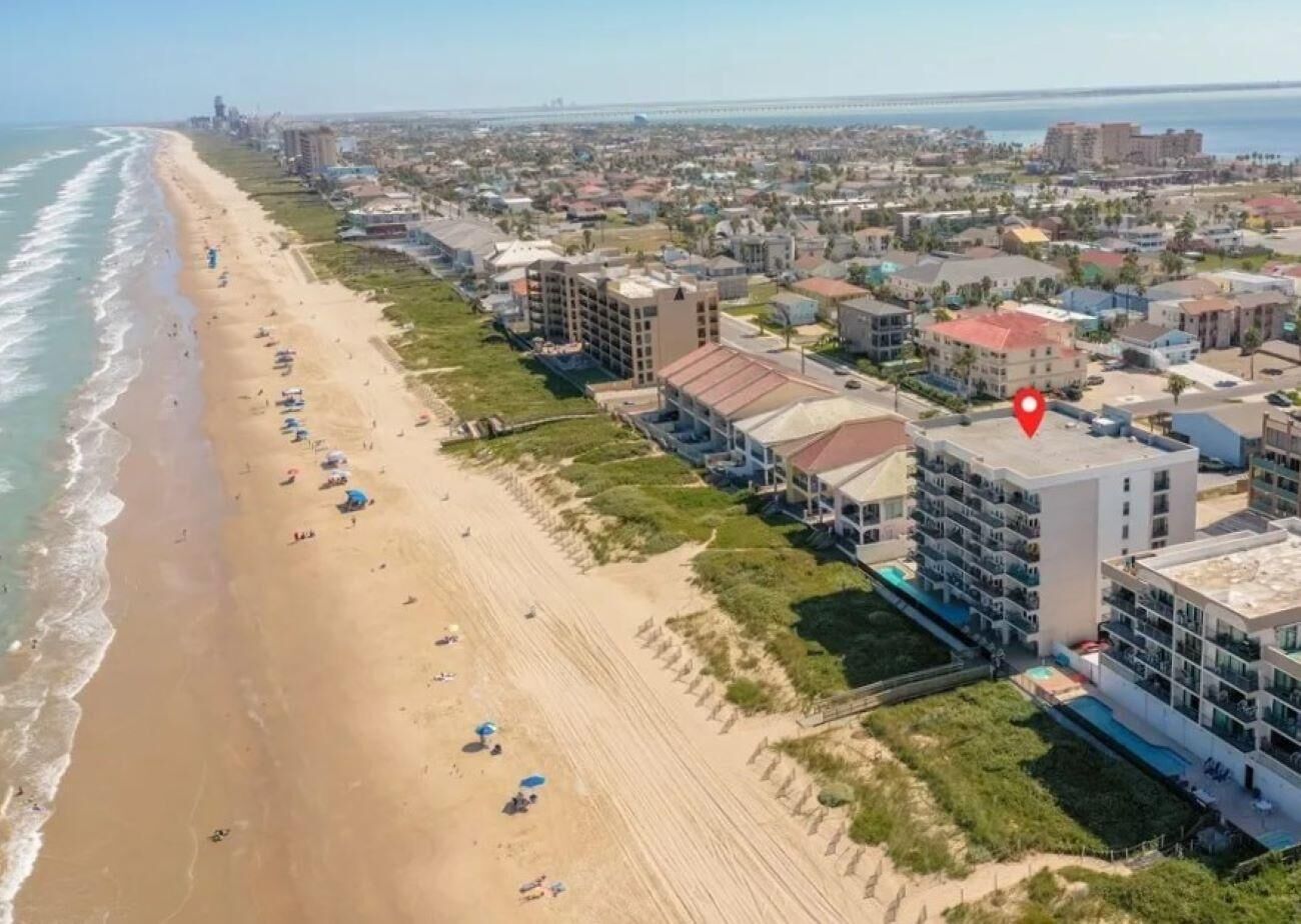 An aerial view of a coastal area with a beach, buildings, and a red location marker.