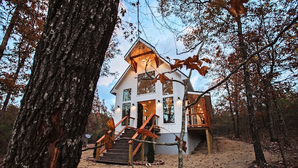 A modern house with a wooden staircase leading to a deck, surrounded by trees.