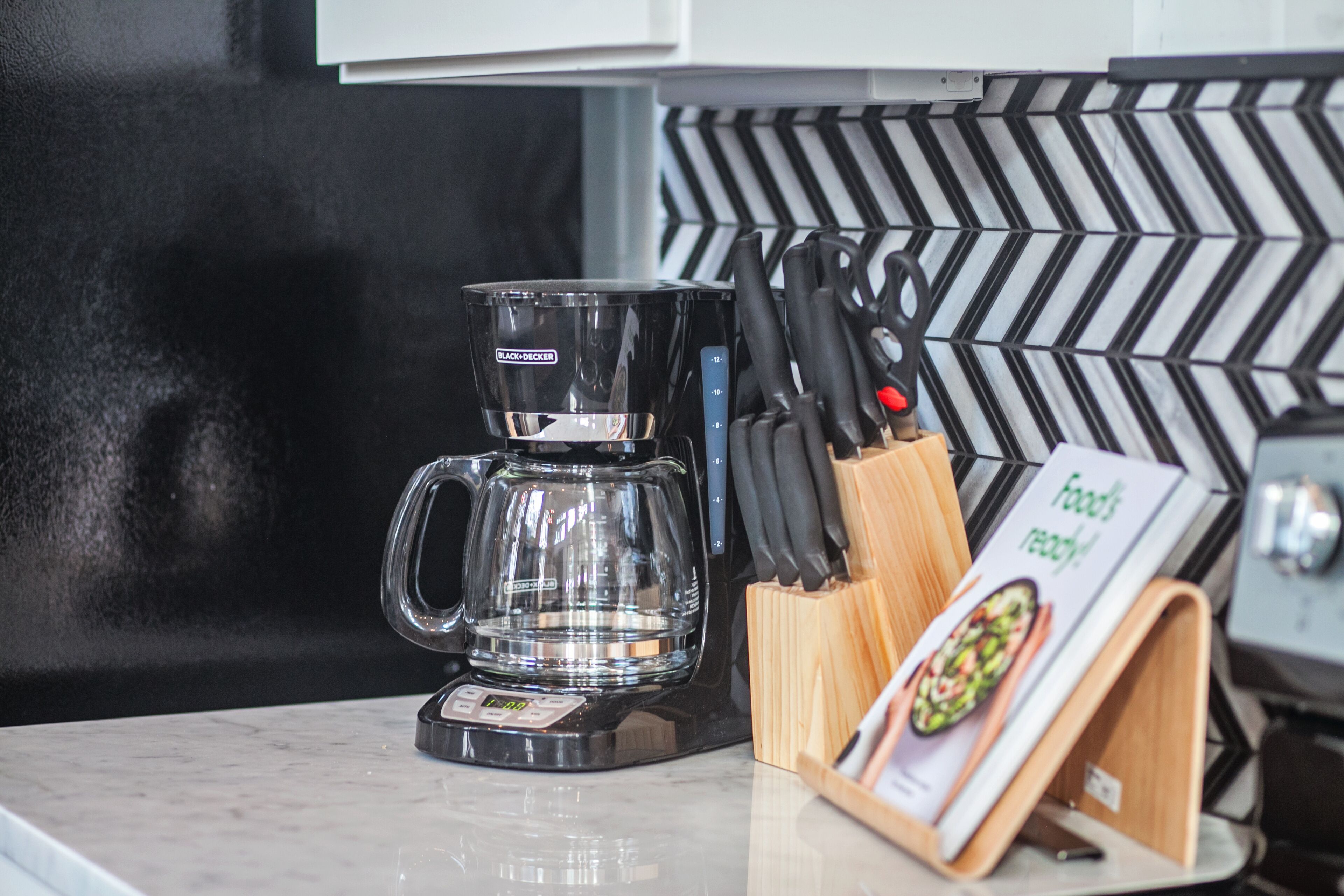 A coffee maker on a kitchen counter with a knife block and a menu stand.