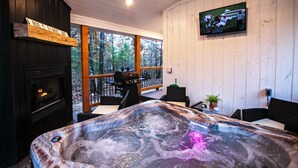 A hot tub with a wooden deck, a fireplace, and a television mounted on the wall.