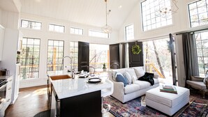 A spacious living area with a large window, a white sofa, a coffee table, and a kitchen area with a marble countertop.