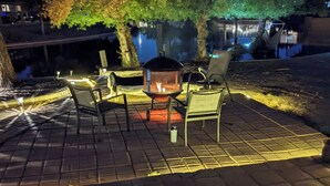 Een terras buiten met een vuurkuil, twee stoelen en een tafel.