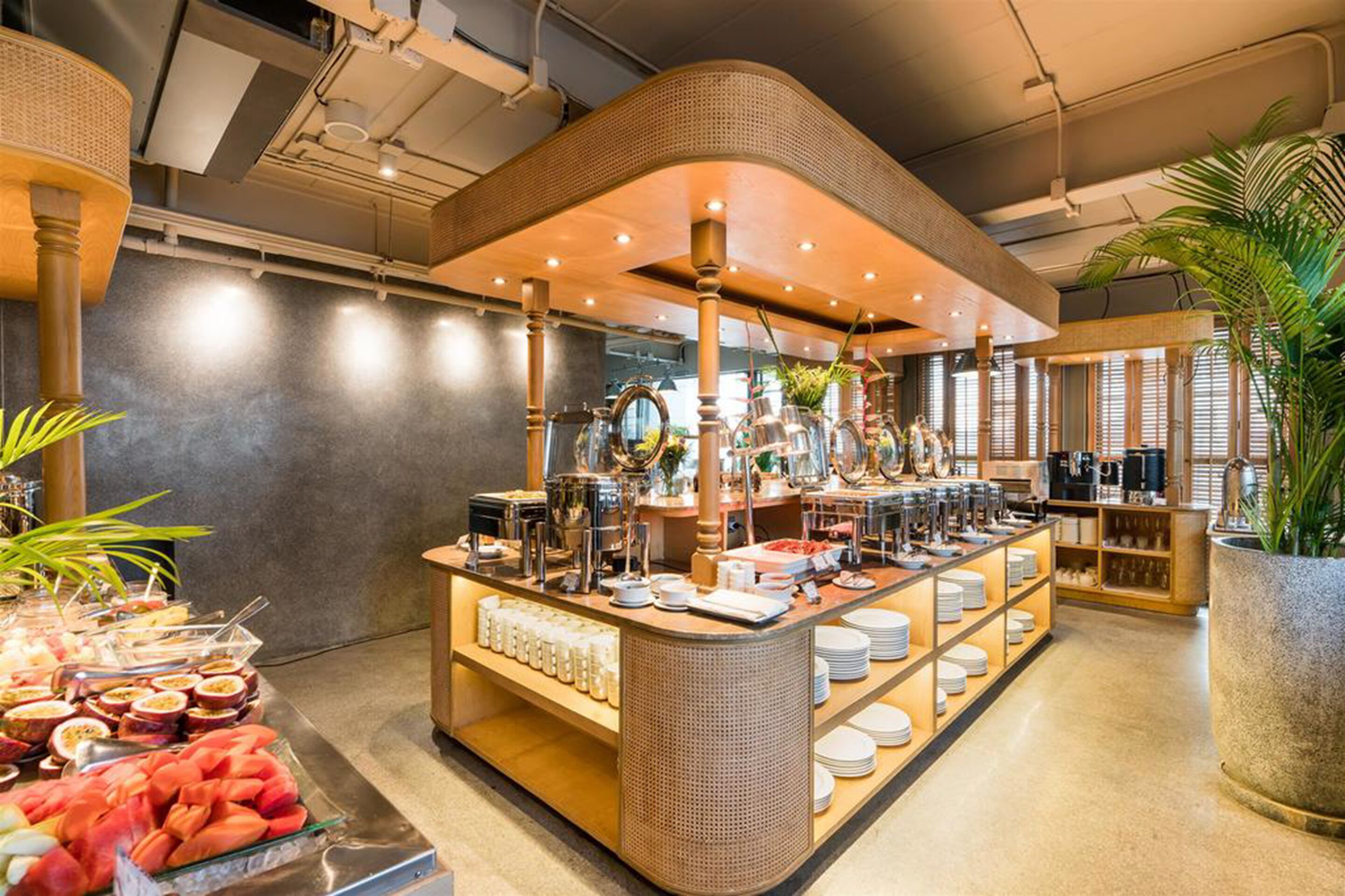 A buffet area with various food items and utensils, a large potted plant, and a modern interior design.