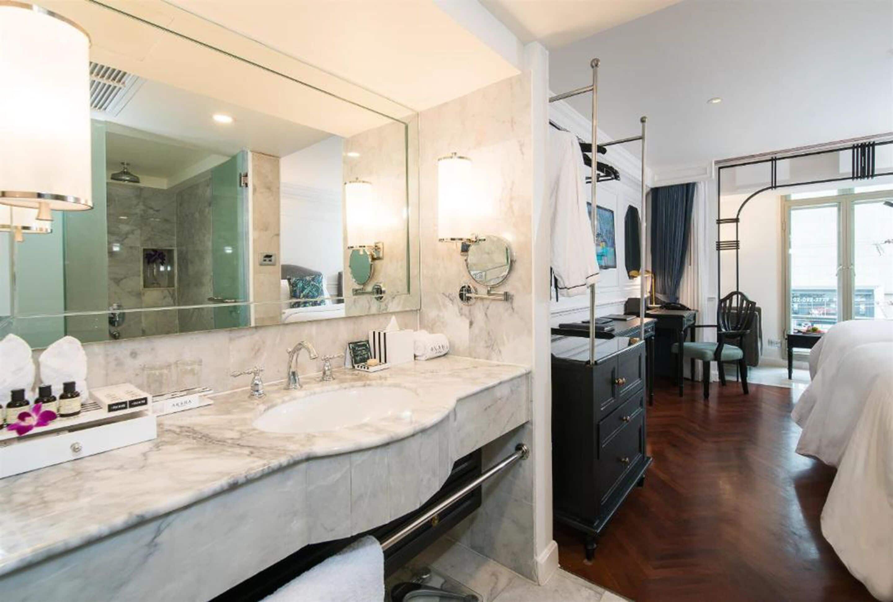 A hotel bathroom with a large mirror, two sinks, and a vanity with a towel rack.
