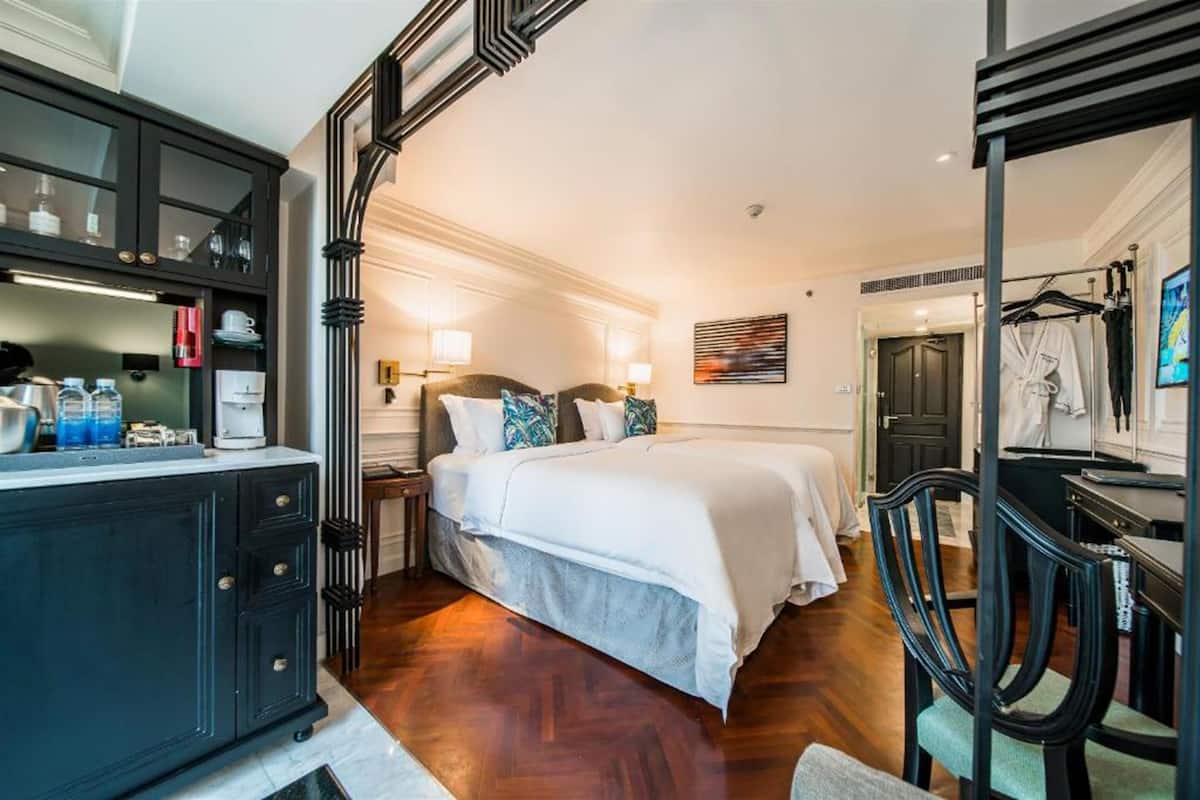 A hotel room with a large bed, a desk with a chair, a wardrobe, and a bathroom visible through an open door.