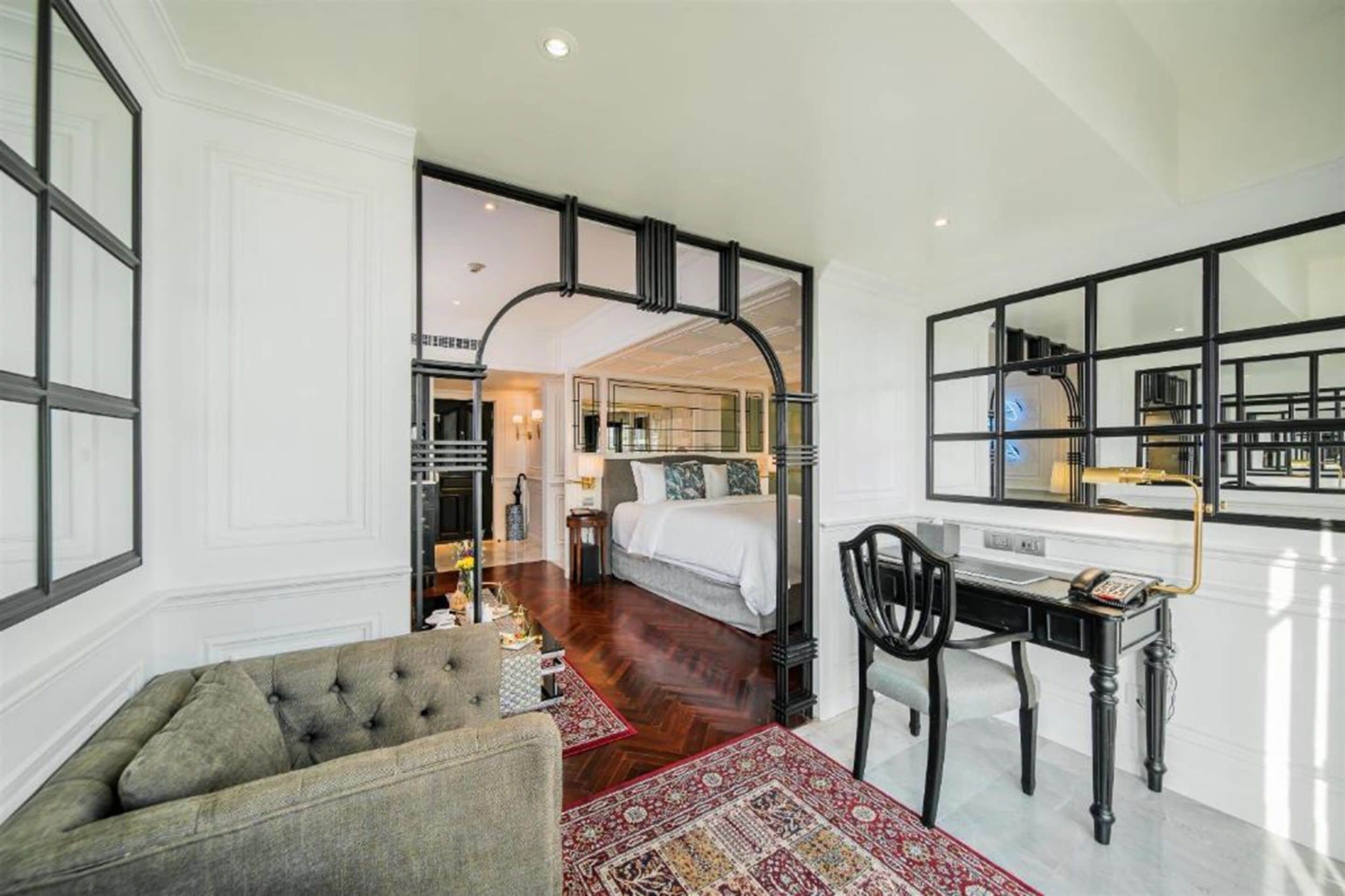 A hotel room with a bed, a desk, a chair, and a large mirror.