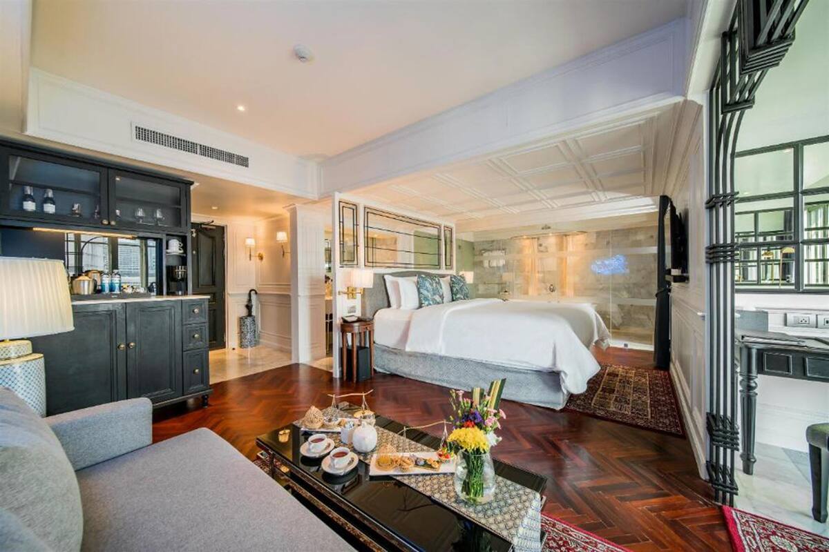 A hotel room with a bed, a sofa, a dining table with a tray of food, and a kitchen area.