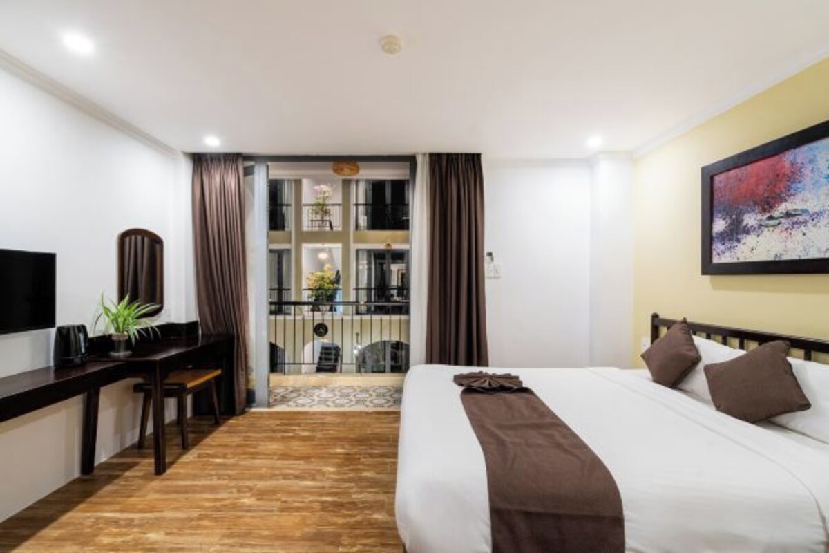 A hotel room with a bed, desk, chair, and a view of the balcony.