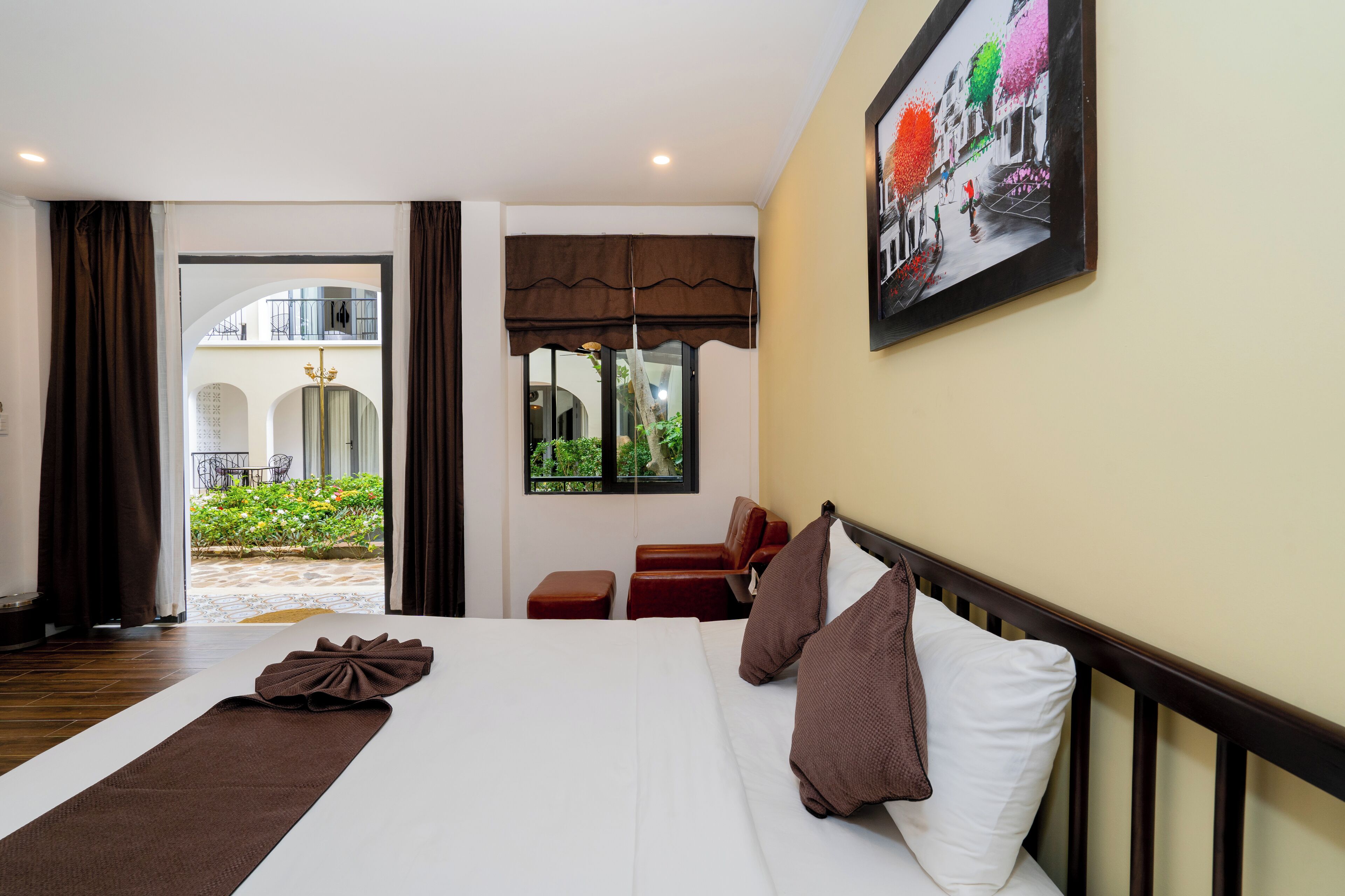 A hotel room with a large bed, a view of the courtyard, and a painting on the wall.