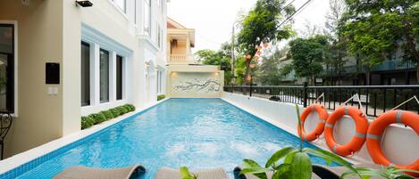 A swimming pool with lounge chairs, a lifebuoy, and a building with a balcony.