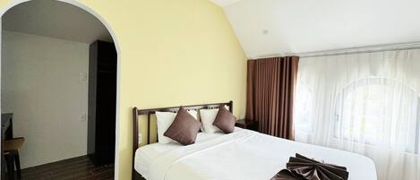 A hotel room with a large bed, a wooden floor, a yellow wall, and a window with curtains.