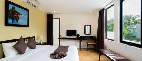 A hotel room with a bed, a desk with a TV, a chair, a bench, and a large window offering a view of the outdoors.