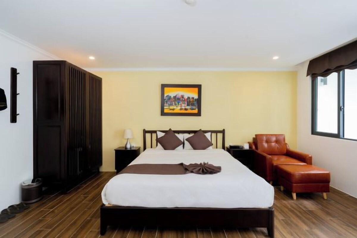 A hotel room with a bed, a chair, a painting, and a wardrobe.