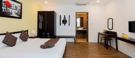 Habitación de hotel con una cama grande, un escritorio, una silla, un espejo, un cuadro en la pared y un baño visible a través de una puerta abierta.